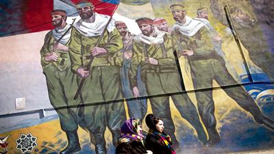 امرأتان في طهران تمرّان قرب لوحة كبيرة تعكس جنوداً إيرانيين أثناء الحرب مع العراق (أ ف ب)