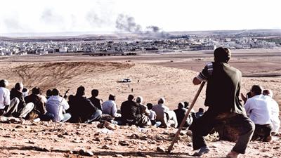 عدد من الأكراد يراقبون القصف الجوي على مدينة كوباني من أعلى تلّة من الجهة التركية (أ ف ب)