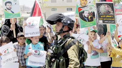 جندي إسرائيلي يقف بالقرب من متظاهرين يحملون لافتات مؤيّدة لأسرى فلسطينيين في سجون إسرائيل بالخليل (إ. بي. أ)
