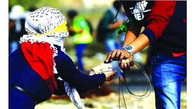 شابة فلسطينية مُلثمة تمد زميلها بالحجارة خلال اشتباكات مع قوات الاحتلال